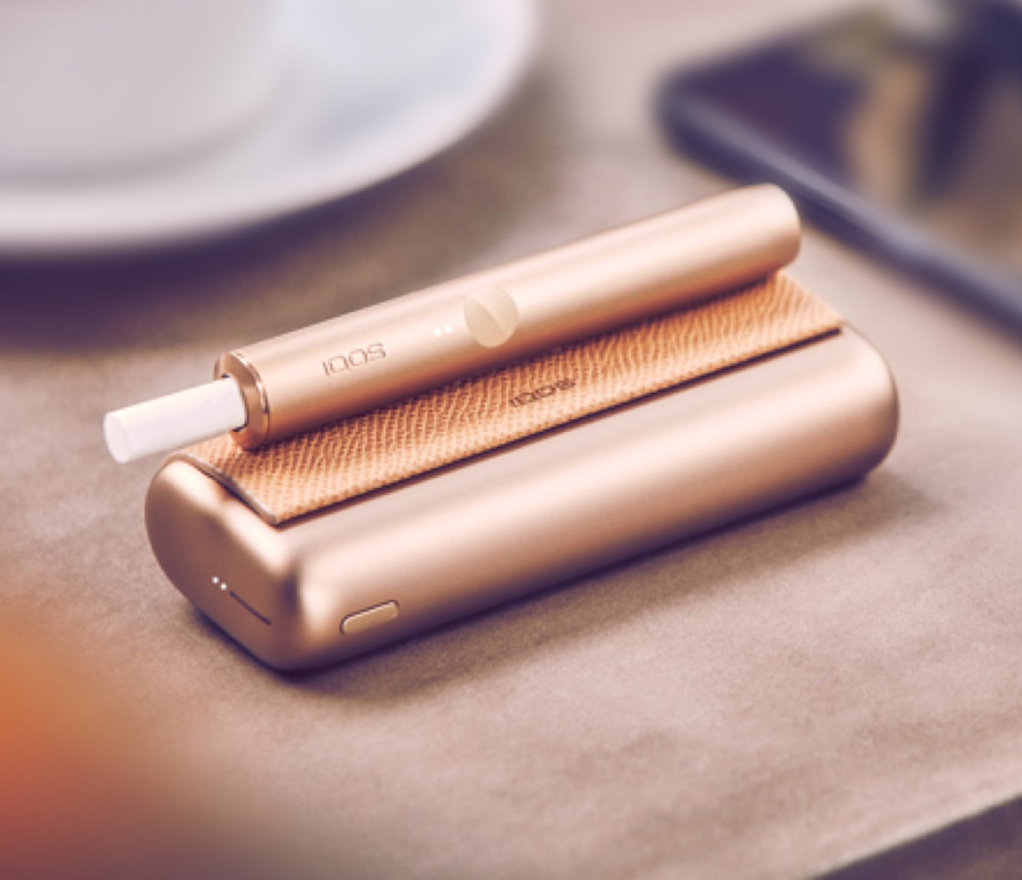 A Gold Khaki IQOS ILUMA PRIME Pocket Charger and Holder on a table.